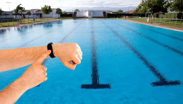 swimmers arm wearing fitbit in front of olympic pool